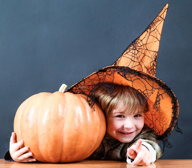 Vacances d'Halloween. Enfant au chapeau de sorcière avec citrouille pointant vers vous. La charité s'il-vous-plaît.