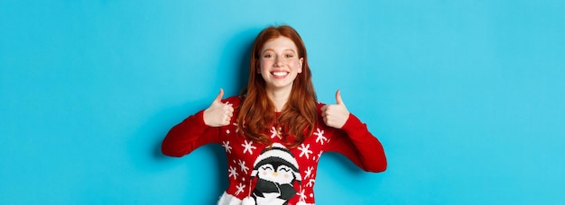 Photo vacances d'hiver et concept de la veille de noël happy smiling girl with red hair montrant les pouces vers le haut en appr