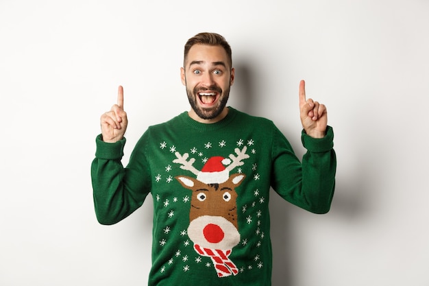 Vacances d'hiver et Noël. Homme excité pointant les doigts vers le haut, montrant une publicité, debout sur fond blanc