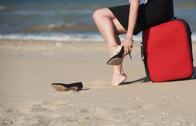 Vacances hors bureau en mer Femme enlève ses chaussures au bord de la mer assise sur la valise