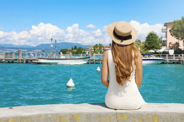 Vacances en Italie. Vue arrière de la belle fille assise sur le mur en profitant de la vue sur le port de Sirmione sur le lac de Garde. Vacances d'été en Italie.