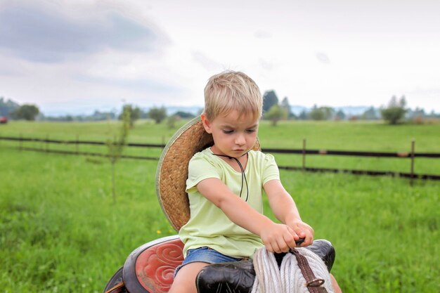 Vacances locales, restez en sécurité, restez à la maison. Petit garçon au chapeau de cowboy jouant dans l'ouest à la ferme parmi les montagnes, été heureux à la campagne, enfance et rêves