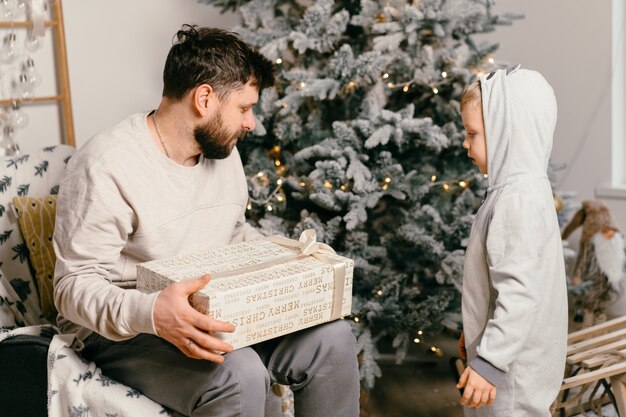 Vacances de Noël beau père jouant avec petit fils mignon près de l'arbre du nouvel an décoré à la maison garçon de tradition familiale donne un cadeau à son père