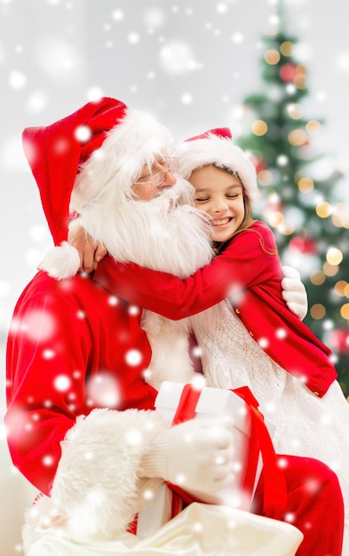 vacances, noël, bonheur et concept de personnes - fille souriante avec boîte-cadeau embrassant le père noël à la maison