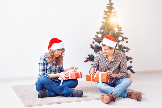 Vacances, noël et concept de famille - Jeune couple heureux ouvrant des cadeaux à la maison.