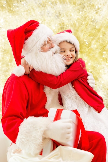 vacances, noël, enfance et concept de personnes - petite fille souriante étreignant le père noël sur fond de feux jaunes