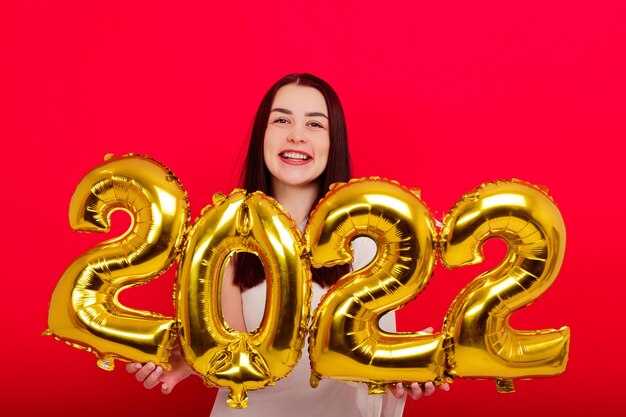 Vacances de Noël - Une jeune femme en robe blanche tient les chiffres 2022 sur fond rouge