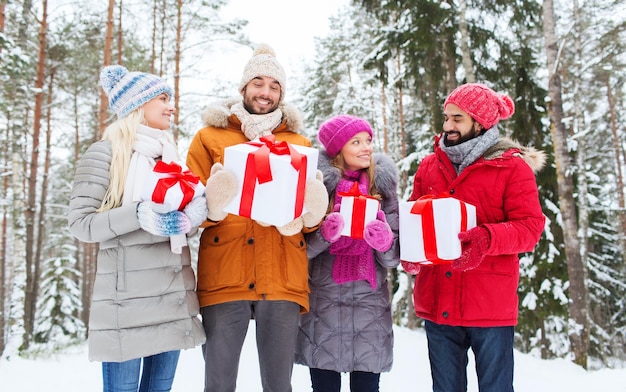 vacances, noël, saison, amitié et concept de personnes - groupe d'amis souriants avec des coffrets cadeaux dans la forêt d'hiver