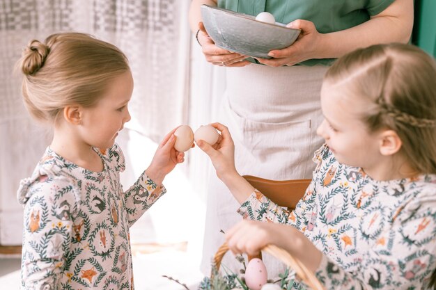 Vacances de Pâques au printemps famille heureuse candide petits enfants sœurs filles ensemble mère maman s'amuser à la maison enchaînement traditionnel jarping ou dumping avec des œufs tradition religieuse