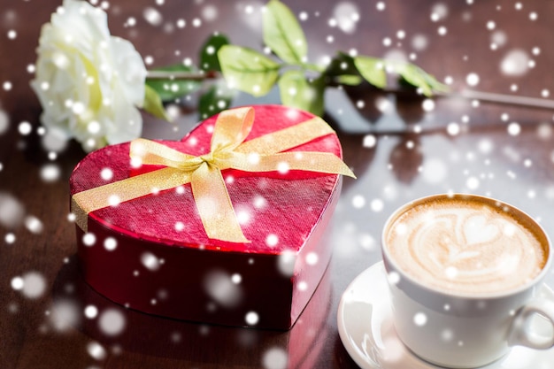 Photo vacances, saint valentin, concept d'amour et de boissons - gros plan d'une boîte cadeau, d'une tasse à café et d'une fleur sur la table au-dessus de la neige