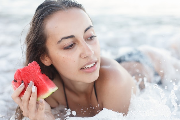 Vacances, station balnéaire, concept touristique - Vacances d'été - jeune fille mangeant de la pastèque fraîche sur la plage de sable. belle jeune femme mange de la pastèque sur la plage aux chaudes journées d'été.