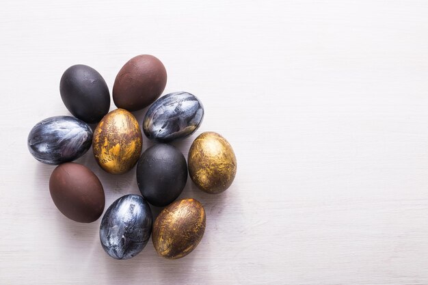 Vacances, traditions et concept de Pâques - Oeufs de Pâques élégants et sombres sur fond de bois blanc avec fond.