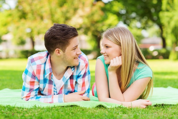 vacances, vacances, concept d'amour et d'amitié - couple souriant allongé sur une couverture et se regardant dans le parc