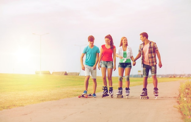 vacances, vacances, concept d'amour et d'amitié - groupe d'adolescents souriants avec patins à roulettes et planche à roulettes à l'extérieur