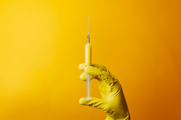 Vaccin contre le coronavirus dans une seringue jaune, un scientifique dans des gants détient une seringue, durcissant pour le durcissement de Covid-19.