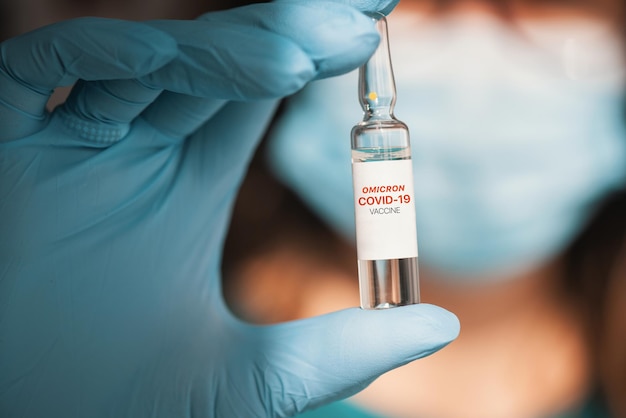 Vaccin omicron modifié par le coronavirus à la main avec des gants de protection bleus