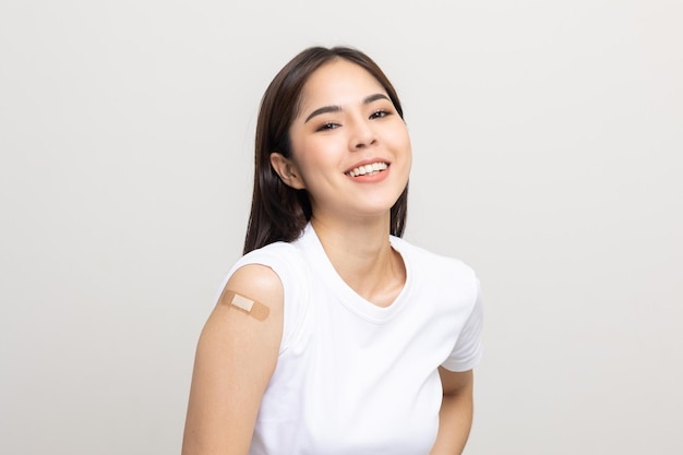 Vaccination. Jeune belle femme asiatique recevant une protection vaccinale contre le coronavirus. Femme heureuse souriante montrant le bras avec un bandage après avoir reçu la vaccination. Sur fond blanc isolé.