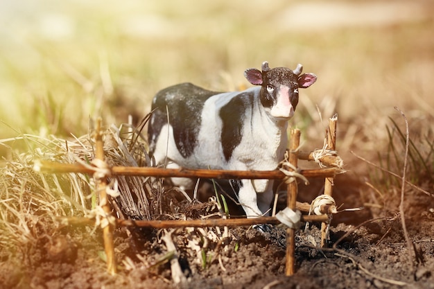 Vache jouet photographiée dans la rue avec une clôture de branches au sol dans l'herbe