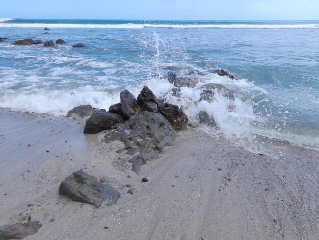 Une vague se brise sur une plage avec l'océan en arrière-plan.