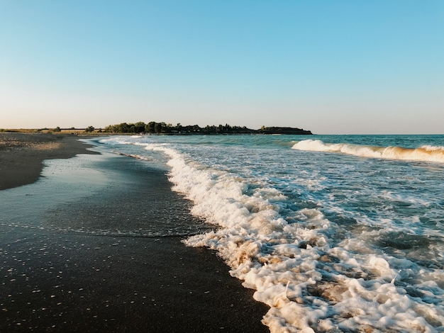Les vagues d'aigue-marine bleue de la mer bordent la plage de sable ensoleillée. vague douce d'écume océanique. ciel de fond naturel