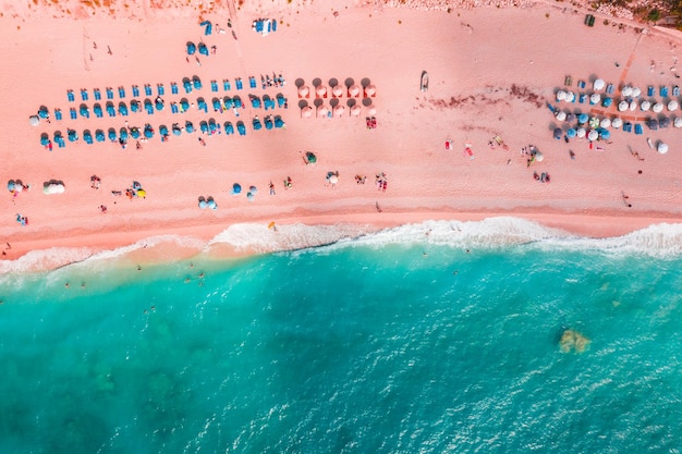 Des vagues bleues douces de la mer avec de la mousse blanche sur une plage de sable tropicale aux tons de corail vivant à la mode de l'année 2019 avec des parapluies tirés d'un drone.