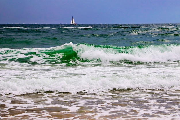 Vagues et côte de l'océanVoilier sur le fondMousse d'eau dans le sable