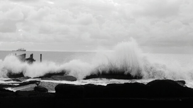 Photo les vagues éclaboussant sur les rochers contre le ciel nuageux