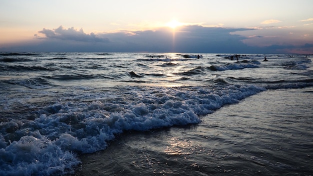 Vagues avec mousse Beau coucher de soleil Des vagues mousseuses roulent sur le rivage sablonneux Vityazevo Anapa Mer Noire Mecque touristique station thermale Nuages colorés dans le ciel du soir Les rayons se reflètent sur l'eau