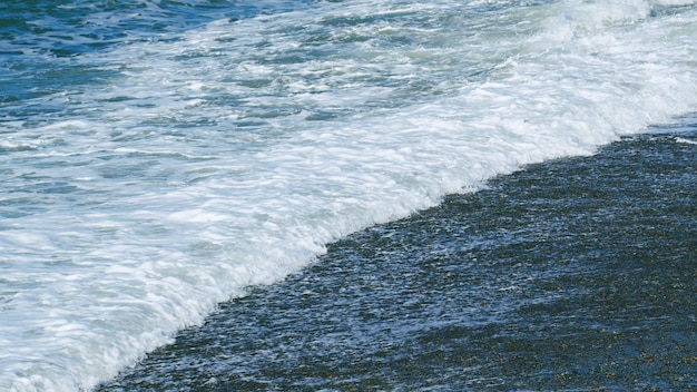 Des vagues de mousse blanche échouant sur le rivage de la mer des cailloux des plages de cailloux de mousse des vagues de mer au ralenti