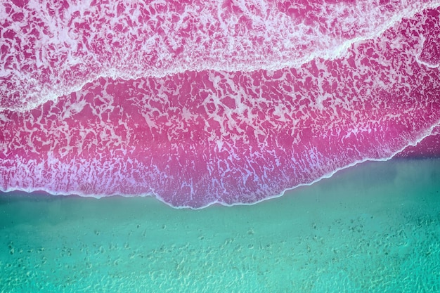 Les vagues roulent sur la plage de sable vue d'en haut de couleur rose bleu artistique