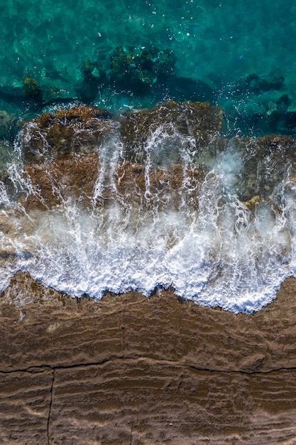 Vagues se brisant sur les rochers des falaises brunes avec marée montante, perspective de drone directement au-dessus