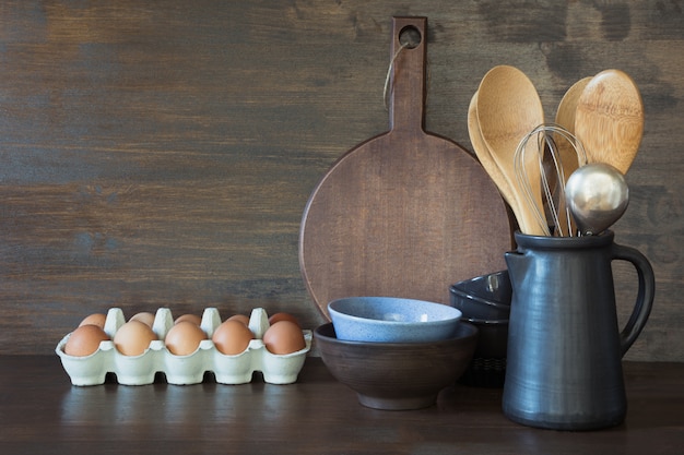 Vaisselle, argile, ustensiles sombres et autres objets divers sur une table en bois.