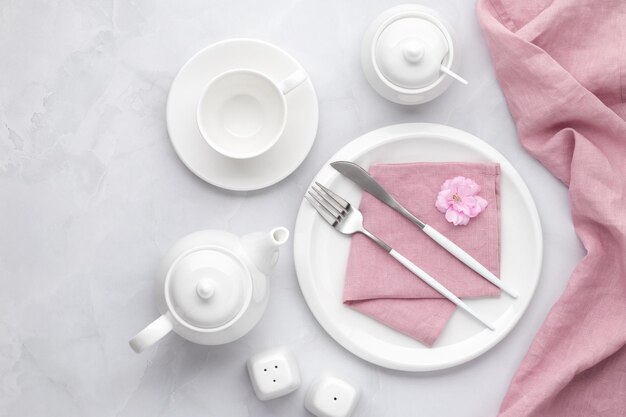 Vaisselle et couverts en céramique blanche Vaisselle, vaisselle, casserole, théière et tasse sur fond de marbre gris Table avec assiette vide, fourchette et couteau Breakfast concept tea party le matin