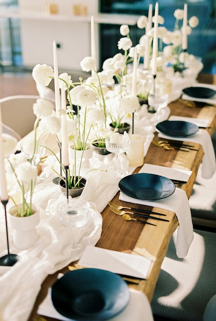 La vaisselle noire se tient sur une table en bois à côté de fleurs blanches et de bougies sur une nappe étroite