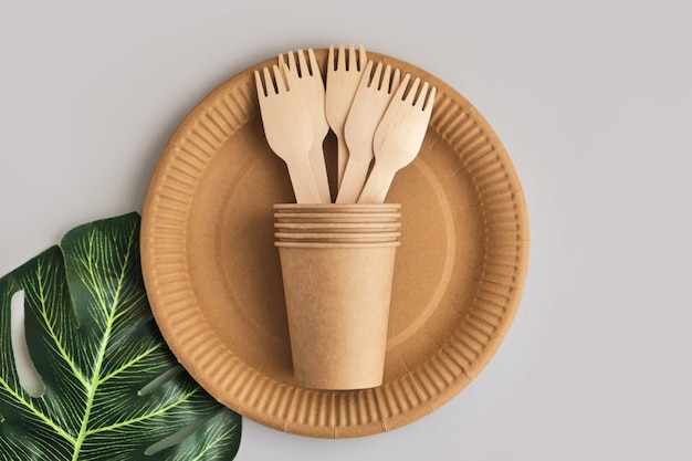 Vaisselle en papier artisanal écologique sur surface grise avec feuille de monstera