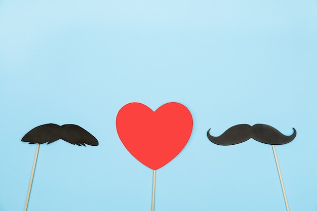 Valentin coeur rouge concept lgbt avec quelques accessoires de moustache papier sur fond bleu