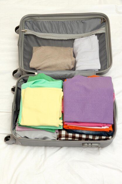 Valise grise ouverte avec des vêtements sur le lit