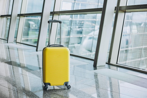 Valise jaune dans la salle d'embarquement de l'aéroport sur fond d'avion. Concept de voyage et de vacances d'été. Valise lumineuse dans la zone d'attente du terminal de l'aéroport.