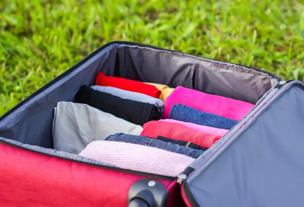 Valise ouverte sur l'herbe verte avec différents vêtements pliés verticalement. Stockage vertical pour un emballage de voyage facile.