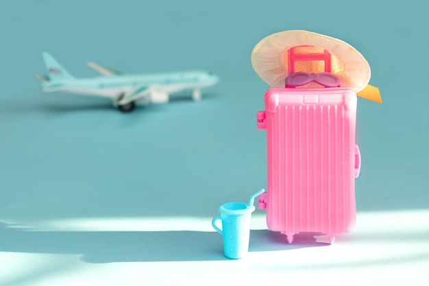 Valise rose avec un chapeau de paille avec un verre de jus dans un rayon de soleil sur fond d'avion au départ