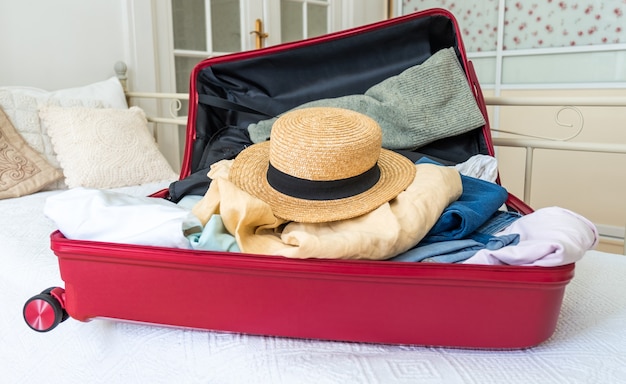 Valise rose sur le lit avec vêtements, chapeau d'été et passeport, prêt pour le voyage.