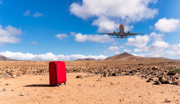 Photo valise rouge au premier plan avec avion atterrissant au-dessus d'un paysage désertique