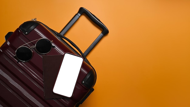 Une valise avec téléphone intelligent et lunettes de soleil sur fond jaune avec espace de copie Préparation pour les vacances d'été