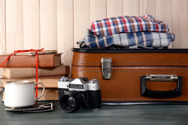 Valise vintage avec des vêtements et des livres sur fond de bois