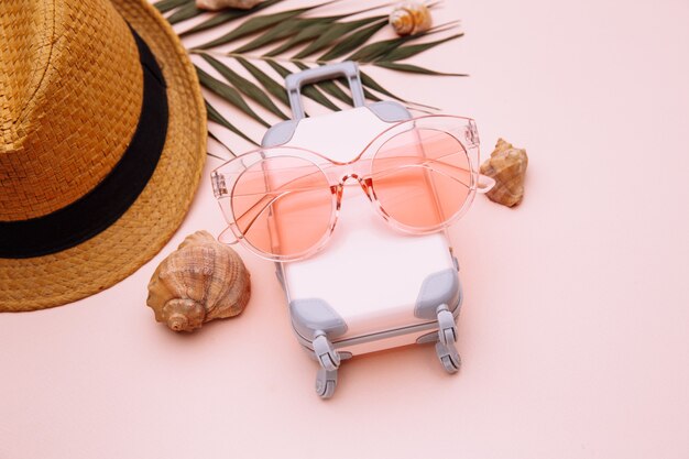 Valise de voyage et lunettes de soleil avec coques sur surface rose. Voyage, vacances d'été ou concept de tourisme