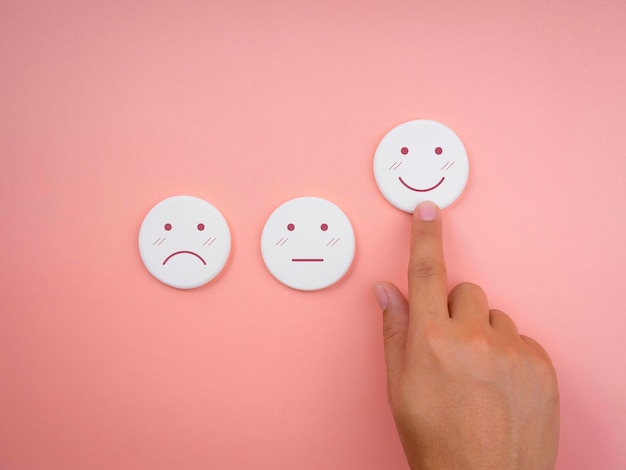 Évaluation du service client, notes, commentaires, expérience client et concepts d'enquête de satisfaction. Main pointant sur le visage souriant heureux sur une éponge ronde blanche sur fond pastel rose.