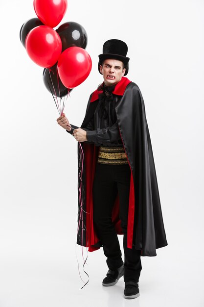 Photo vampire halloween concept - portrait complet de beau vampire caucasien en costume d'halloween noir et rouge.