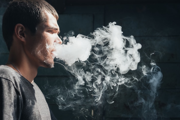 Vape man. le jeune moderne produit des nuages de vapeur