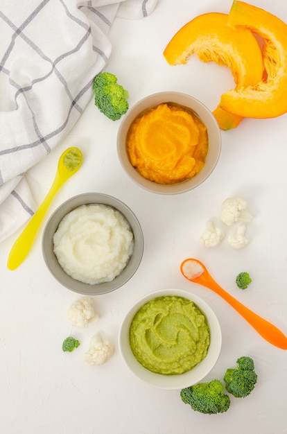 Variation des trois purées de légumes maison en bols. Purée de potiron, purée de chou-fleur et purée de brocoli sur fond blanc.