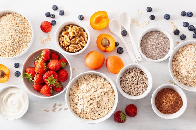 Variaty de céréales brutes, fruits et noix pour le petit déjeuner. Flocons d'avoine et coupe en acier, orge, noix, chia, abricot, fraise. Ingrédients sains